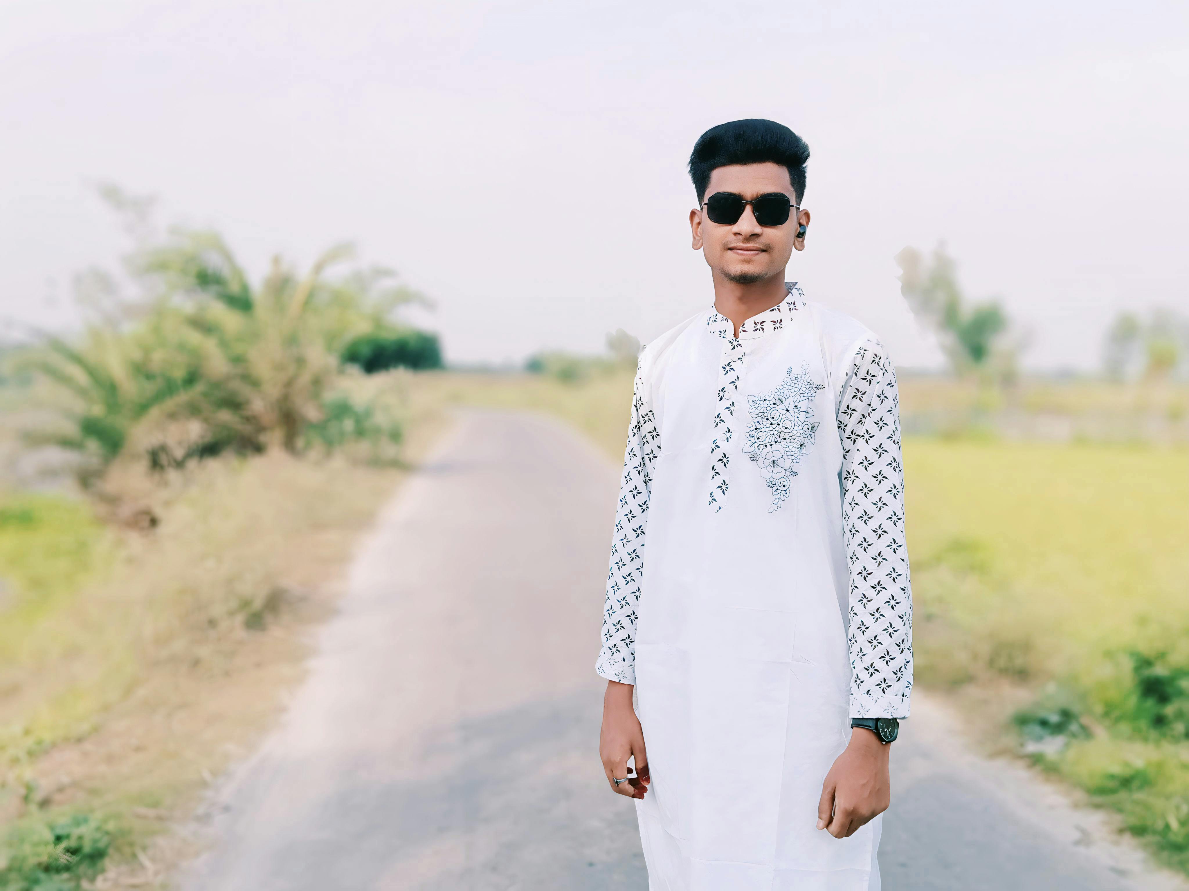 Portrait of a young man wearing sunglasses and traditional white clothing on a sunny rural road.