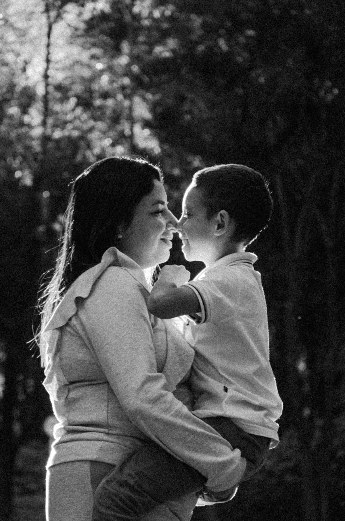 Smiling mother hugging her son in a sunlit forest