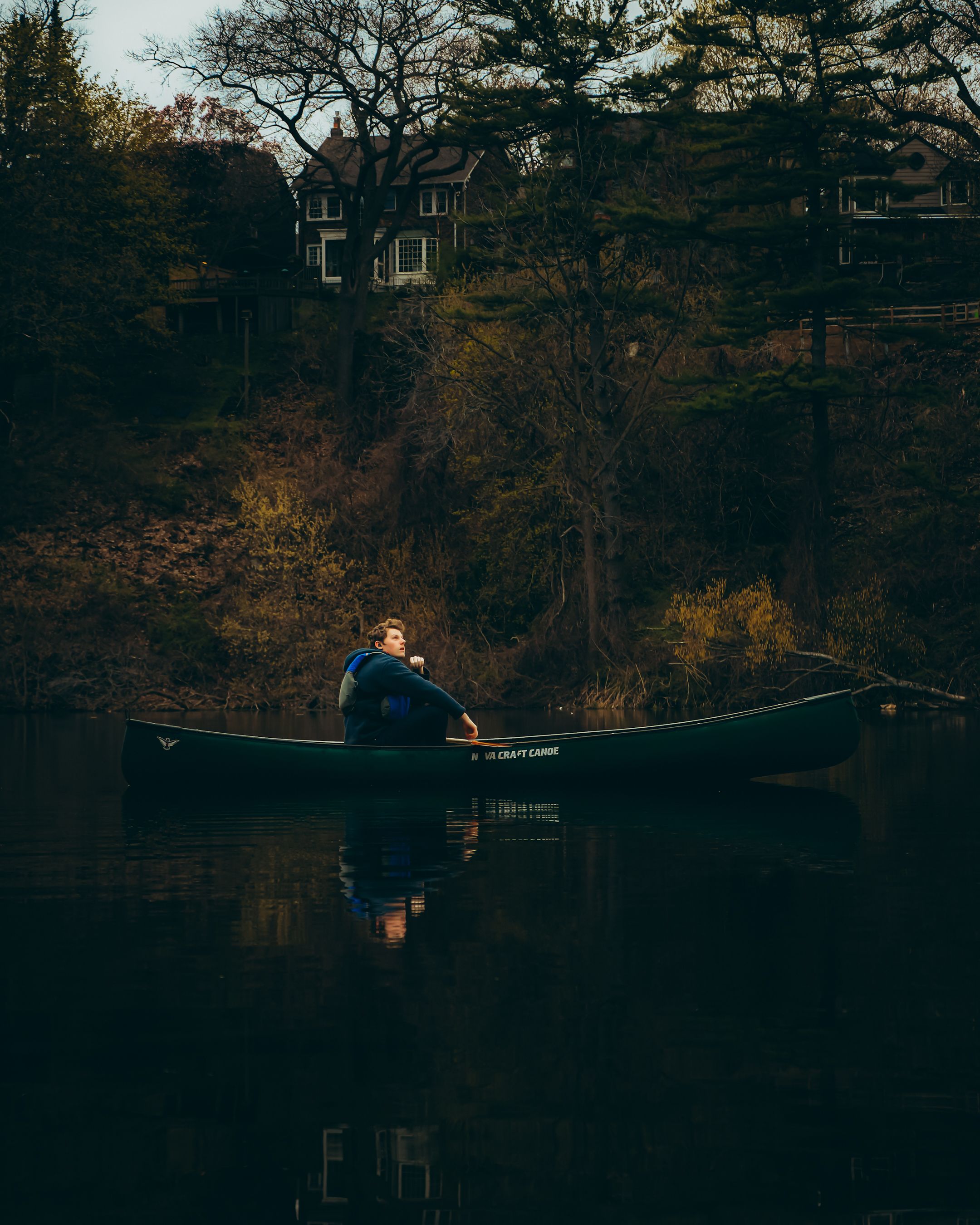 A man enjoys a peaceful canoe ride on a river with autumn trees in Toronto, Canada.