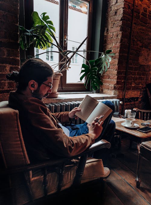 Man Reading a Book While Listening to Music on Wireless Earphones