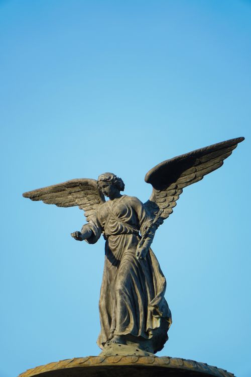 Free Elegant statue of an angel with wings spread wide against a clear blue sky. Stock Photo