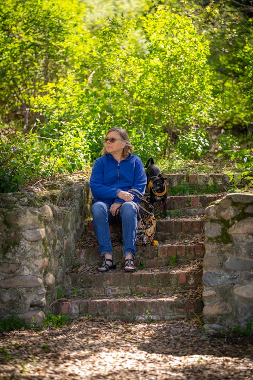 Woman With a Small Black Dog on a Walk Sitting on the Stairs in the Park