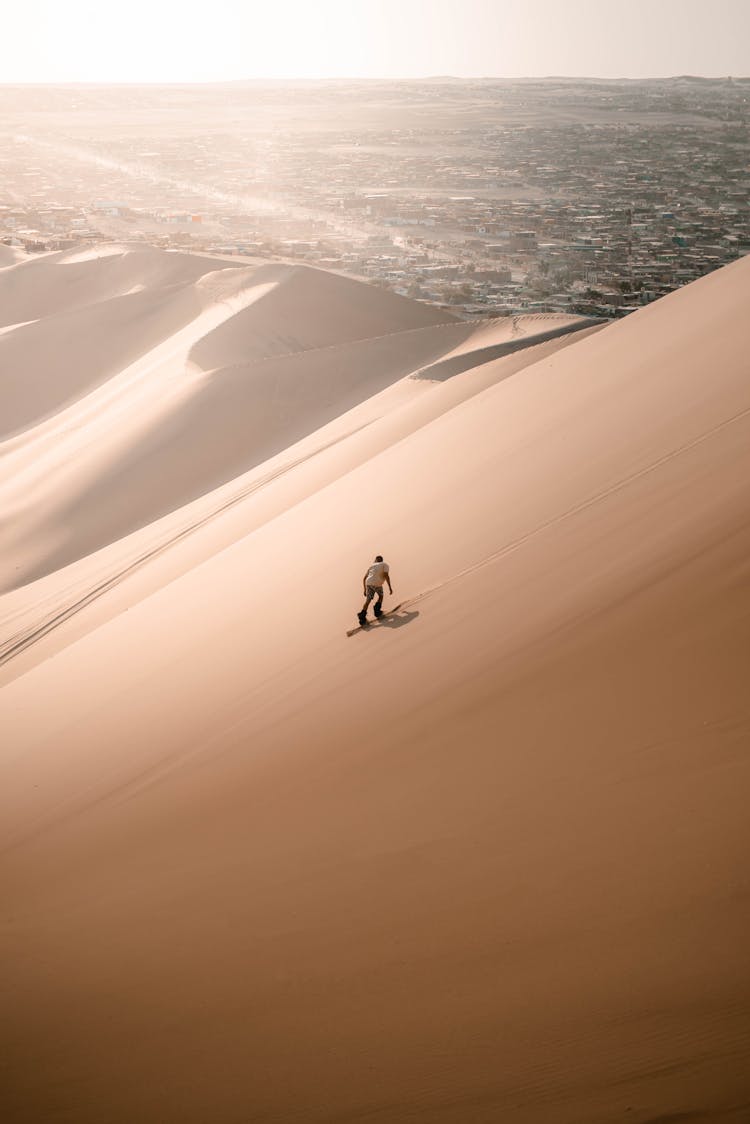 Man Sliding On Desert Dunes Near Town