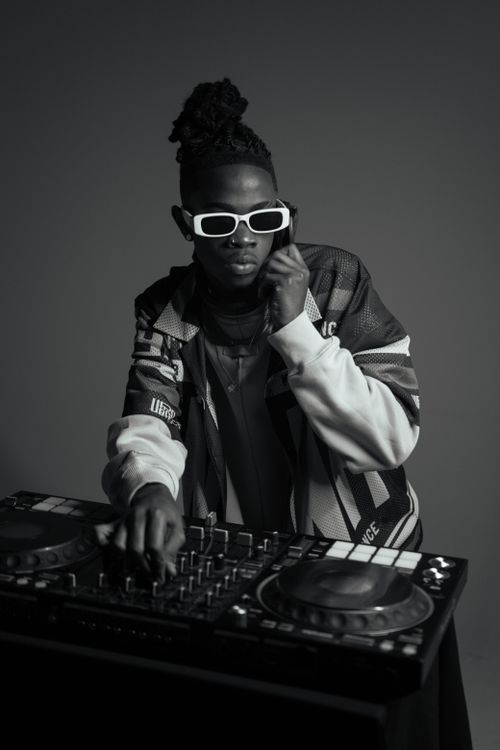 Free DJ with dreadlocks and sunglasses mixing music on a turntable in studio. Stock Photo
