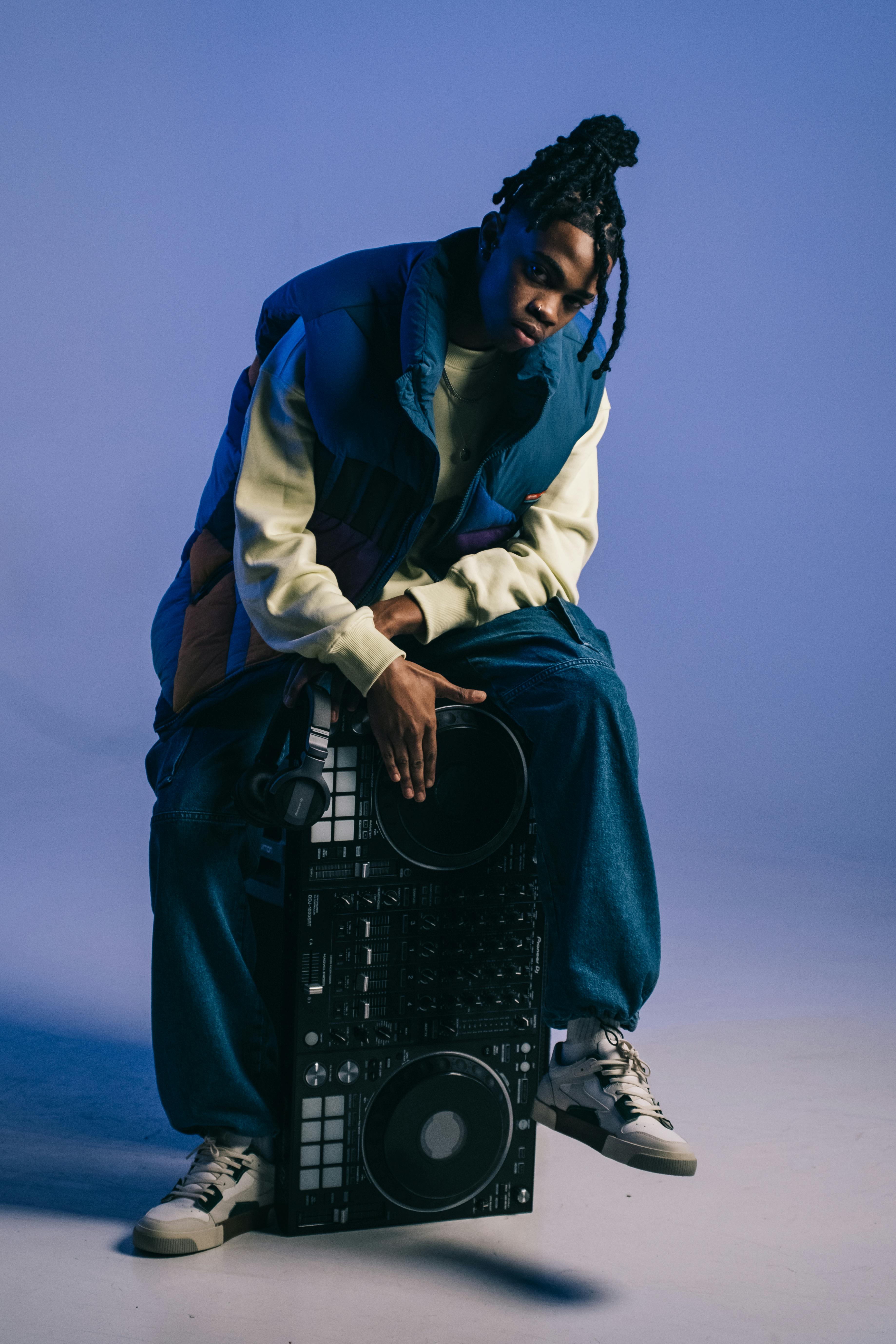 Portrait of a fashionable DJ sitting with sound mixer in a studio setting, showcasing modern music culture.