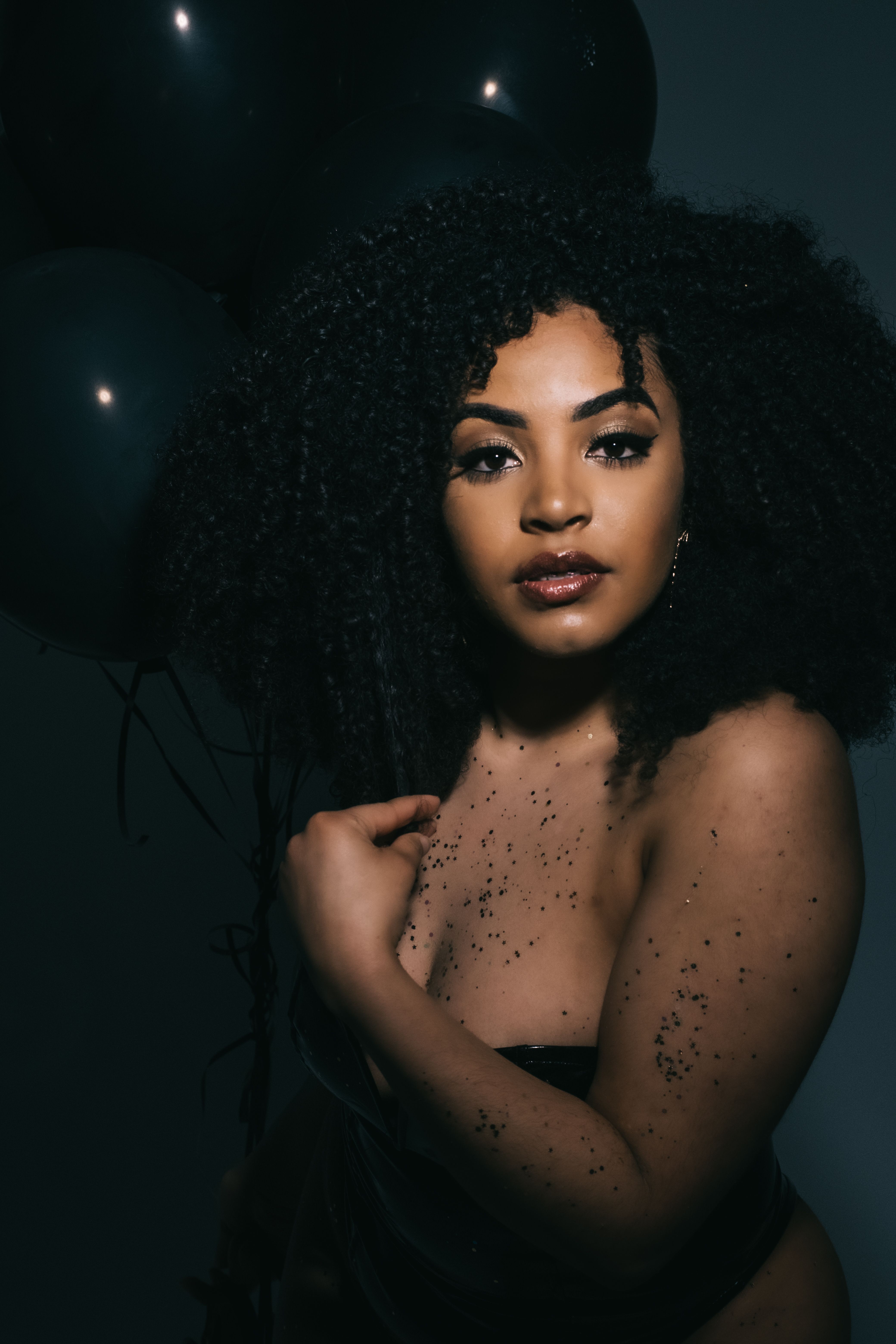 Stunning portrait of a woman with curly hair and glitter against a dark background.
