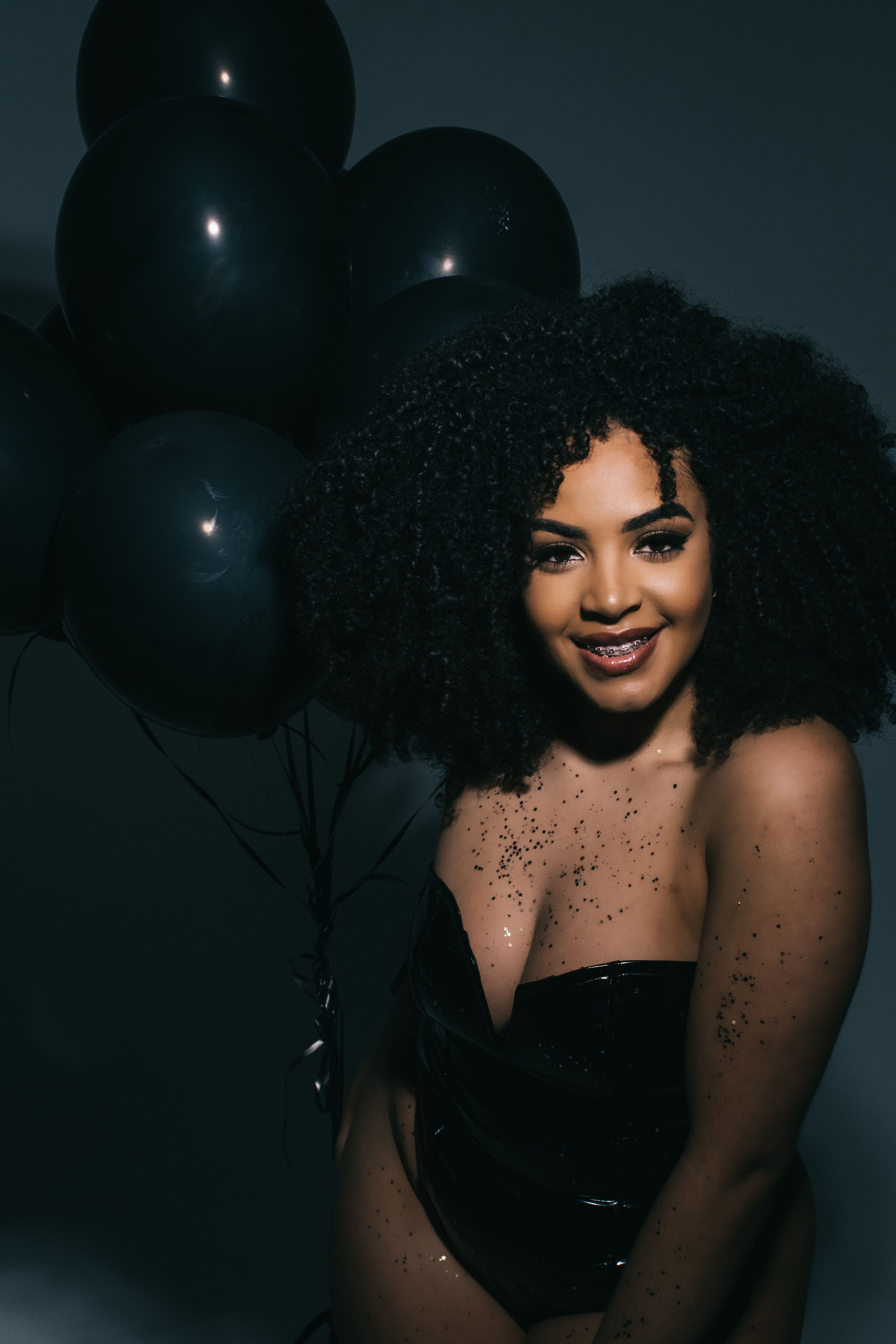 Glamorous portrait of a smiling woman with black balloons against a dark background.