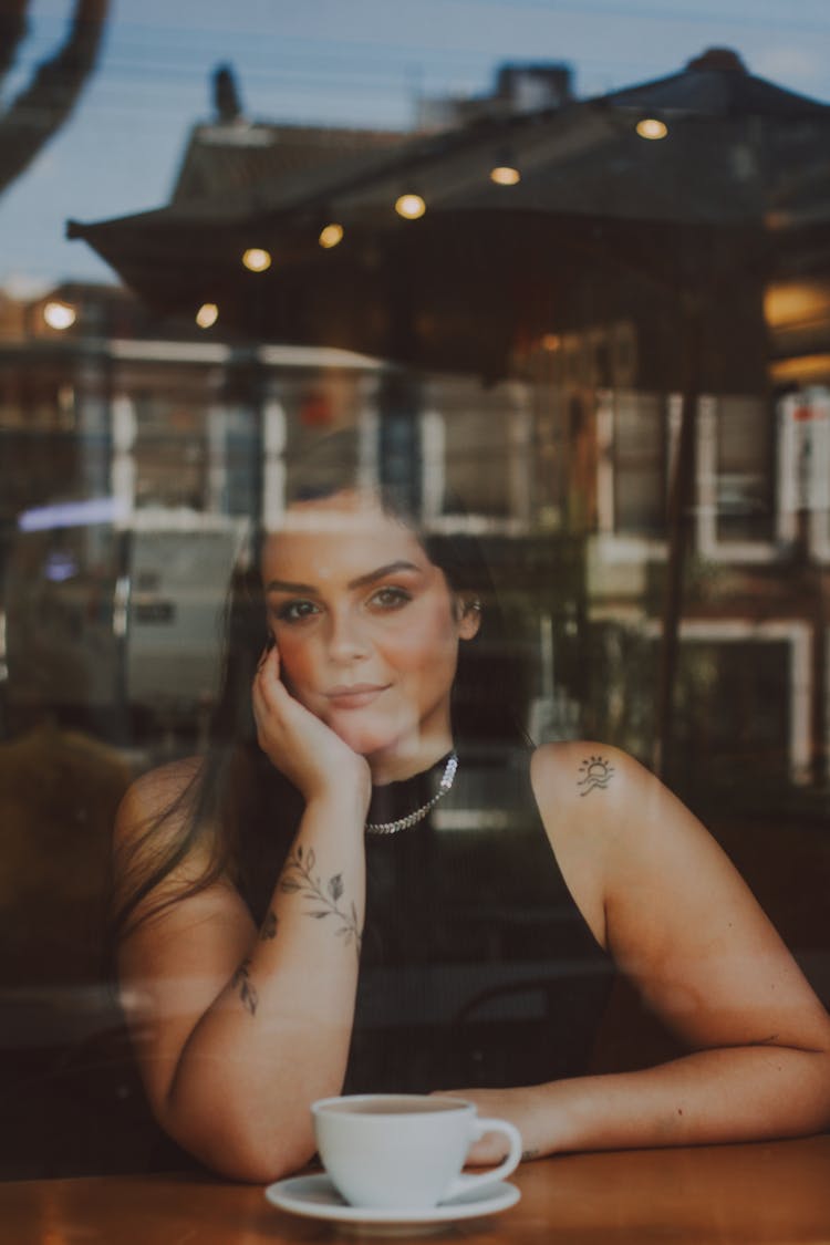 Woman Sitting With A Cup Of Coffee Behind The Glass