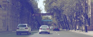 汽车行驶在绿树成荫的城市街道上，街道两旁有建筑物和标志