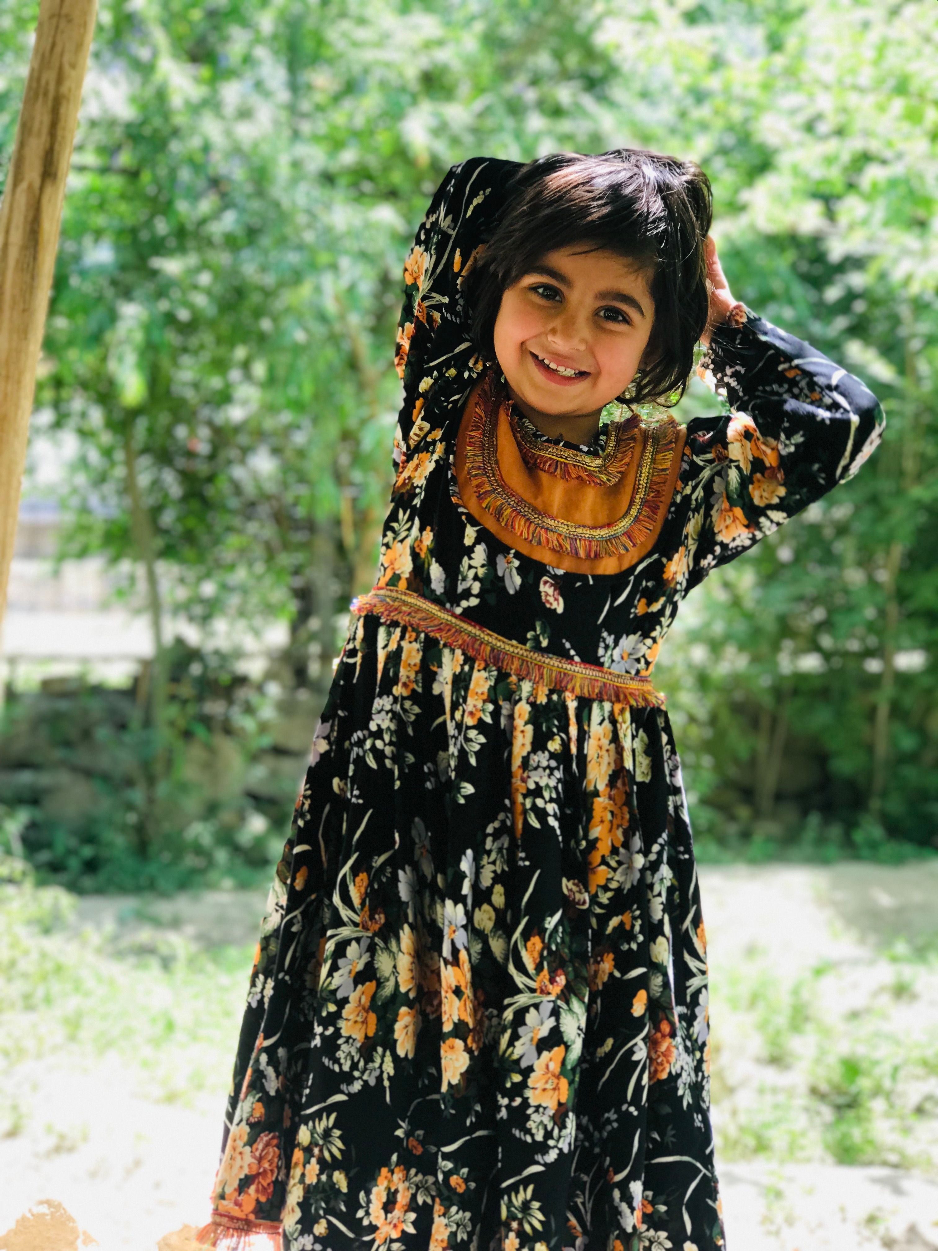 Cheerful girl in a floral black dress standing outdoors, smiling joyfully.