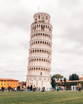 The iconic Leaning Tower of Pisa stands tall against a lively backdrop of tourists and green lawns.