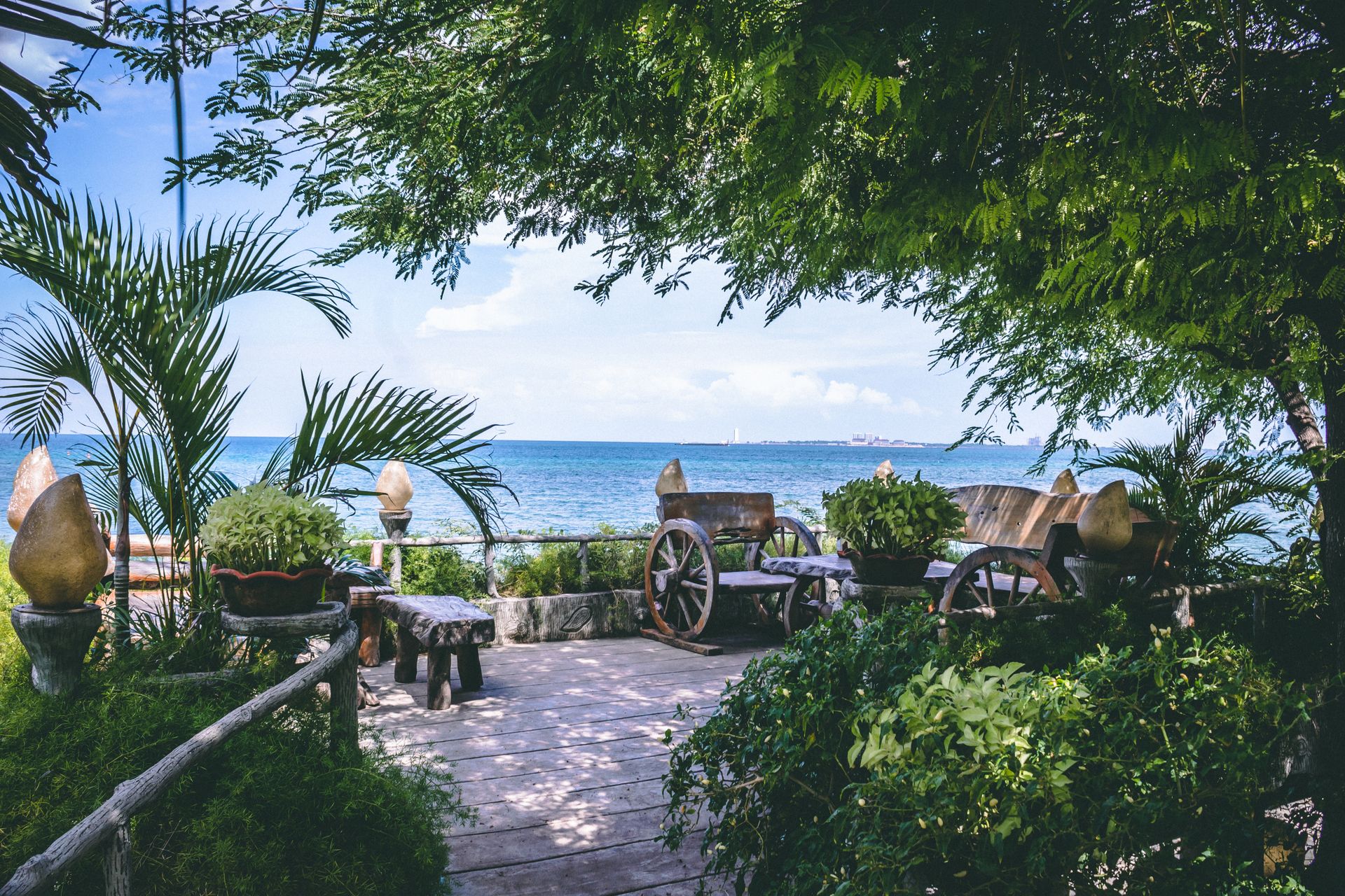 Serene garden overlooking a calm ocean view, framed by lush greenery and rustic benches.