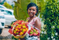 A cheerful woman poses outdoors holding colorful flower bouquets, exuding joy.