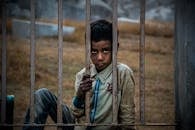 一个表情严肃的男孩坐在户外生锈的栅栏后，透出一种沉思的感觉