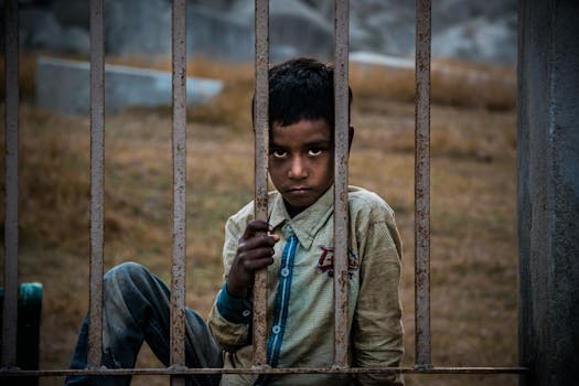 一个表情严肃的男孩坐在户外生锈的栅栏后，透出一种沉思的感觉