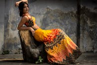 一位女士穿着五彩斑斓的民族服装，优雅地坐在树桩上