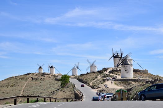 Scenic view of historic windmills on a hill in Consuegra, Spain, under a bright blue sky.
