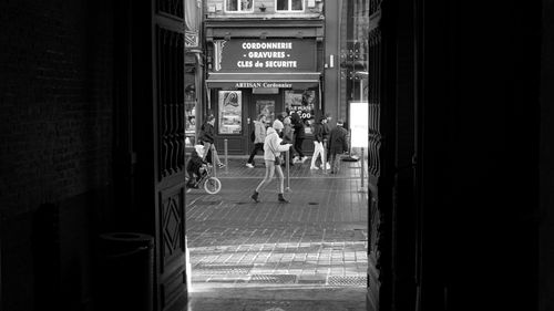 Free Monochrome image of pedestrians on a city street, framed by a doorway. Stock Photo