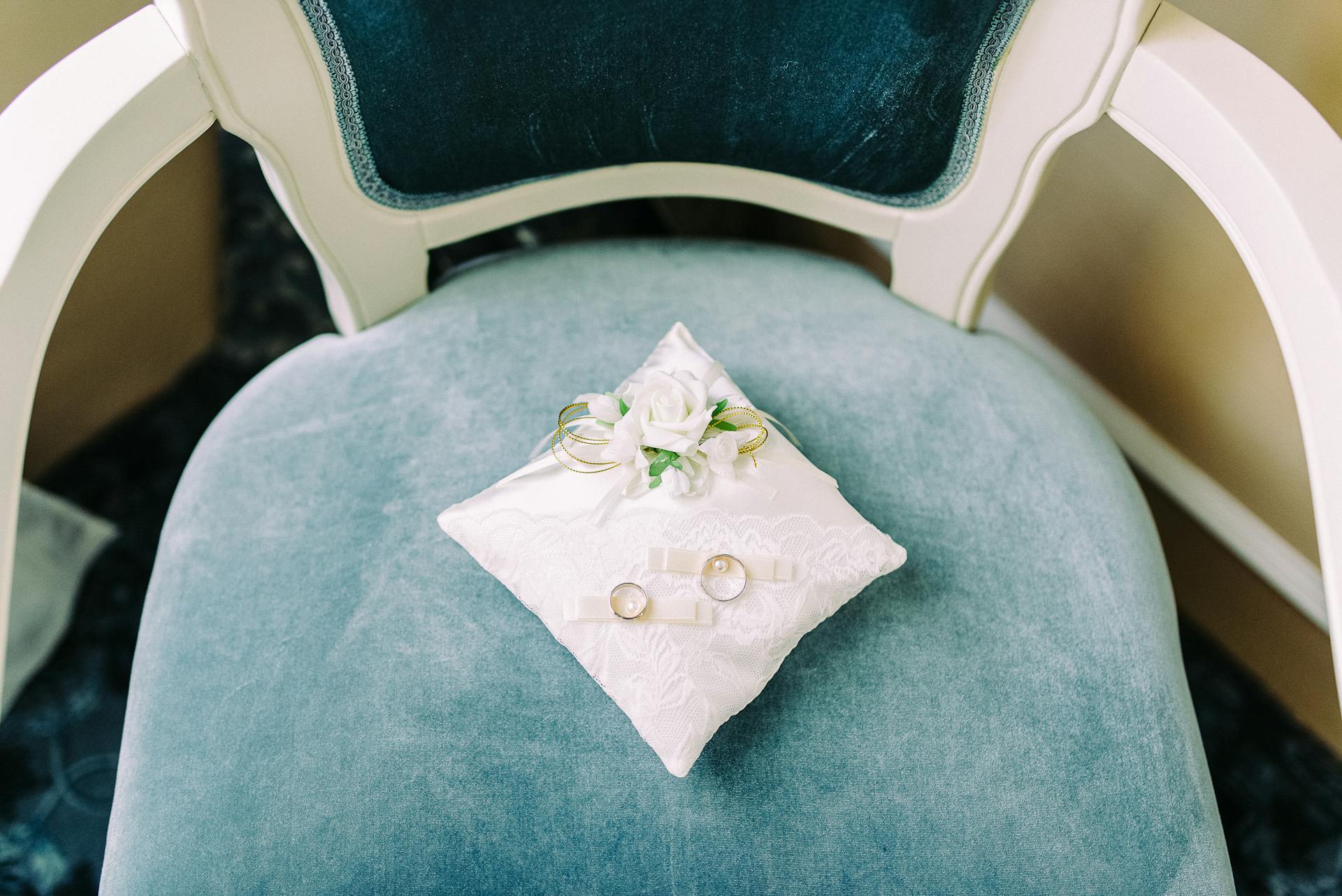 Close-up of wedding rings on a white pillow placed on a blue chair, capturing elegance and romance.