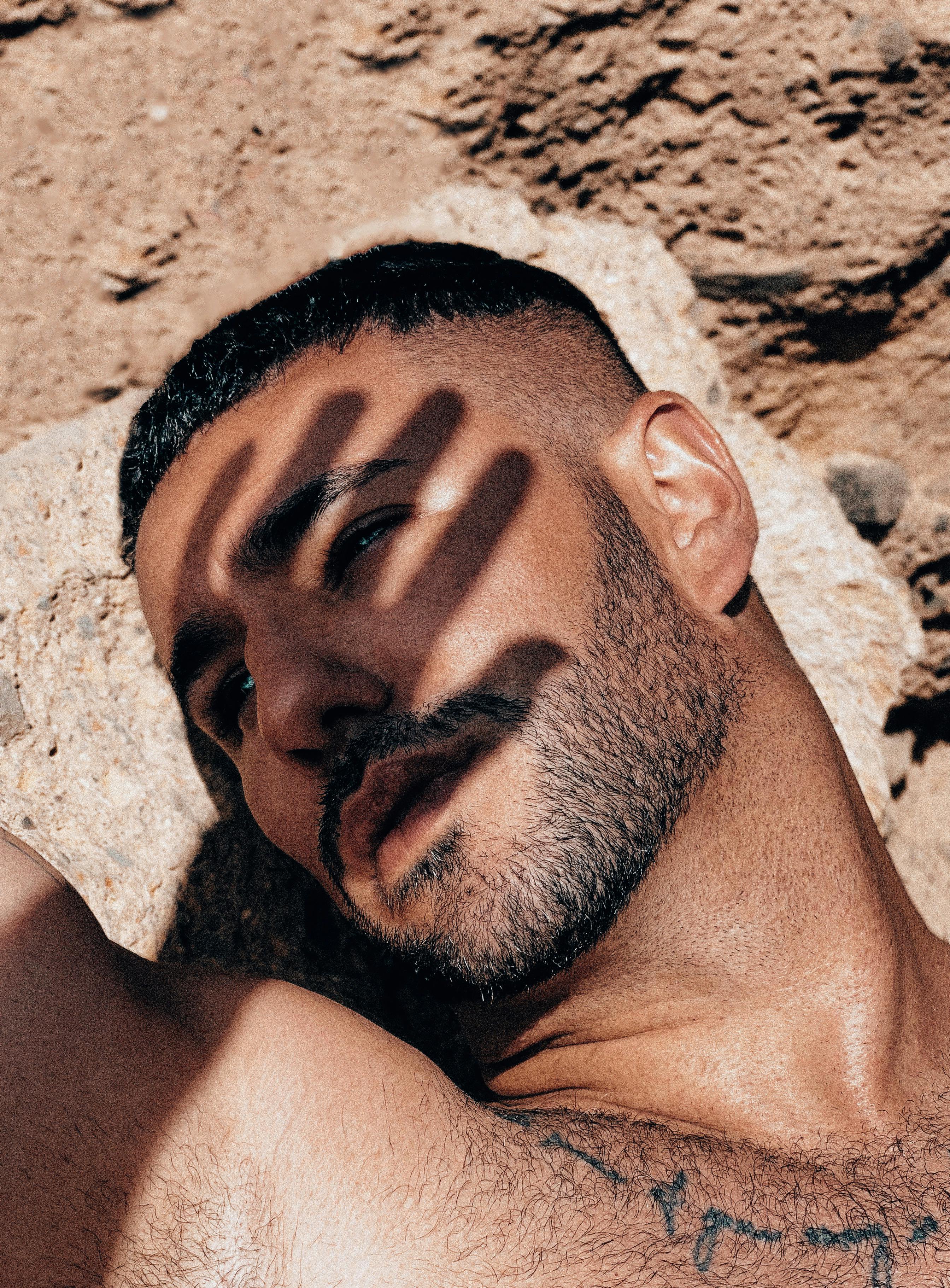 Close-up of a man with a beard under sunlight, casting a hand shadow on his face.