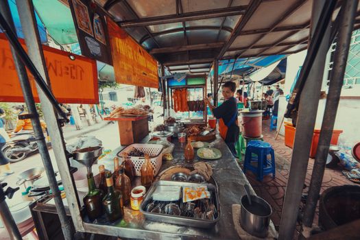 A bustling food stall in Bangkok with a friendly vendor and variety of dishes.