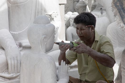 A skilled sculptor working on a marble Buddha statue, focusing on intricate details.