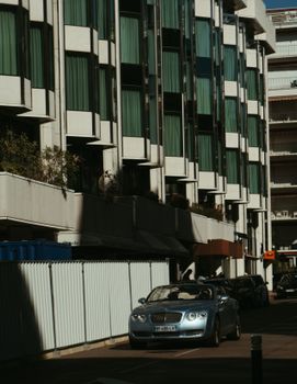 A Bentley Continental parked near modern buildings in sunlit Cannes, France, exuding urban elegance.