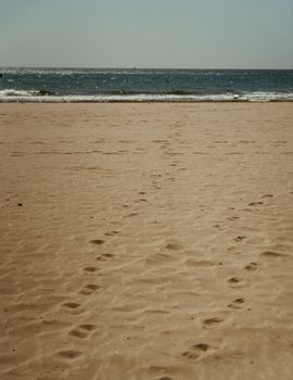 Serene sandy beach with footprints leading to the sea under a clear sky, Barcelona.