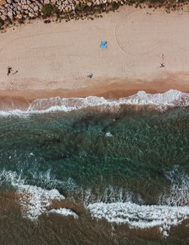 Drone shot capturing the picturesque beach in Barcelona with clear waves and scattered beachgoers.
