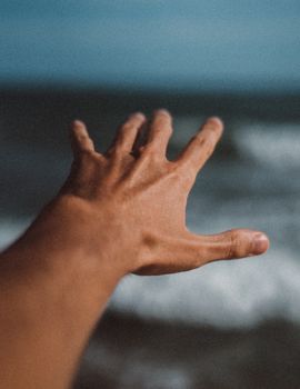 Close-up view of a hand reaching towards ocean waves, capturing a moment of serenity and freedom.