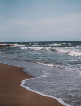Peaceful waves crash on a scenic, empty Barcelona beach under a blue sky.