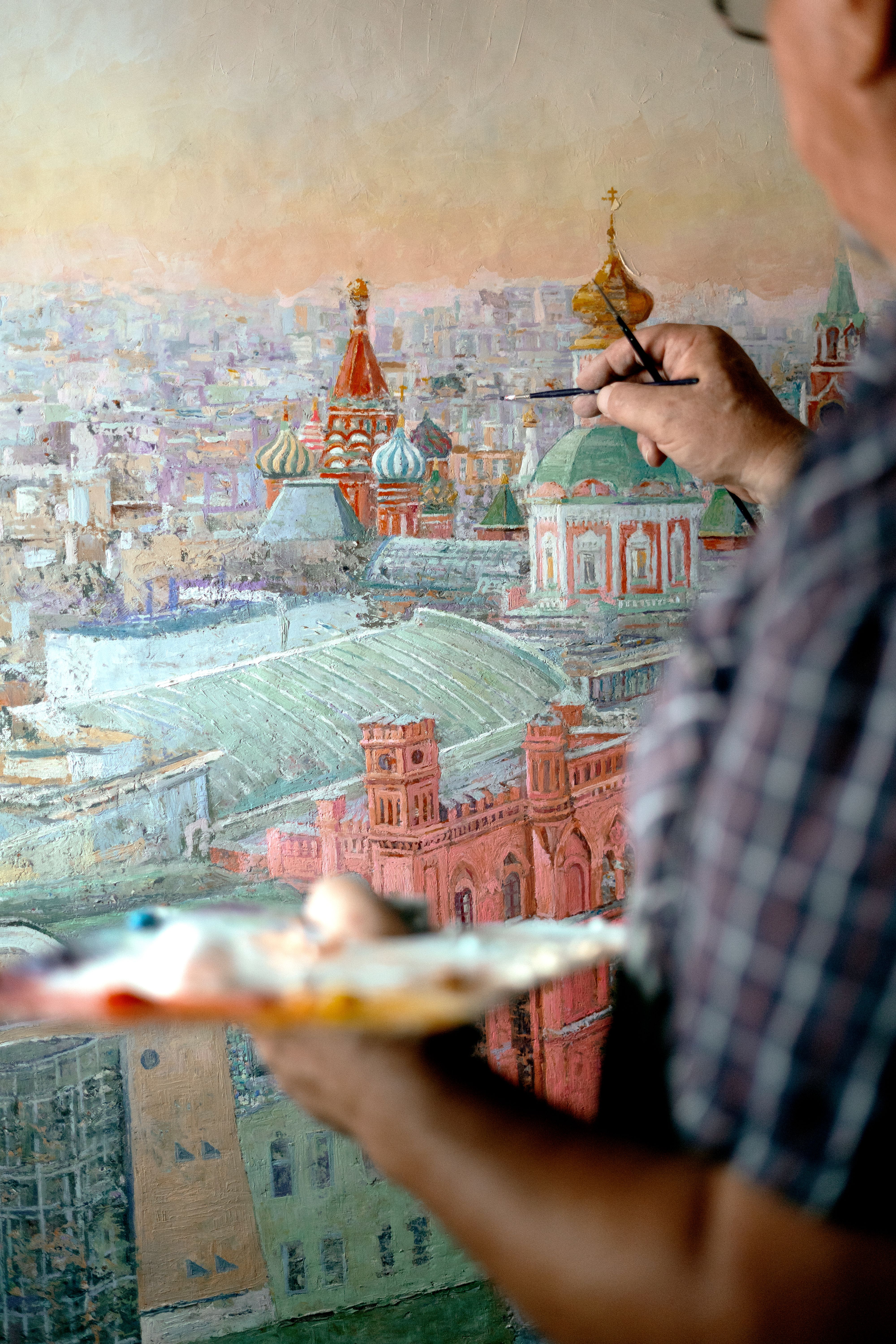 Close-up of an artist painting a cityscape featuring domed rooftops.