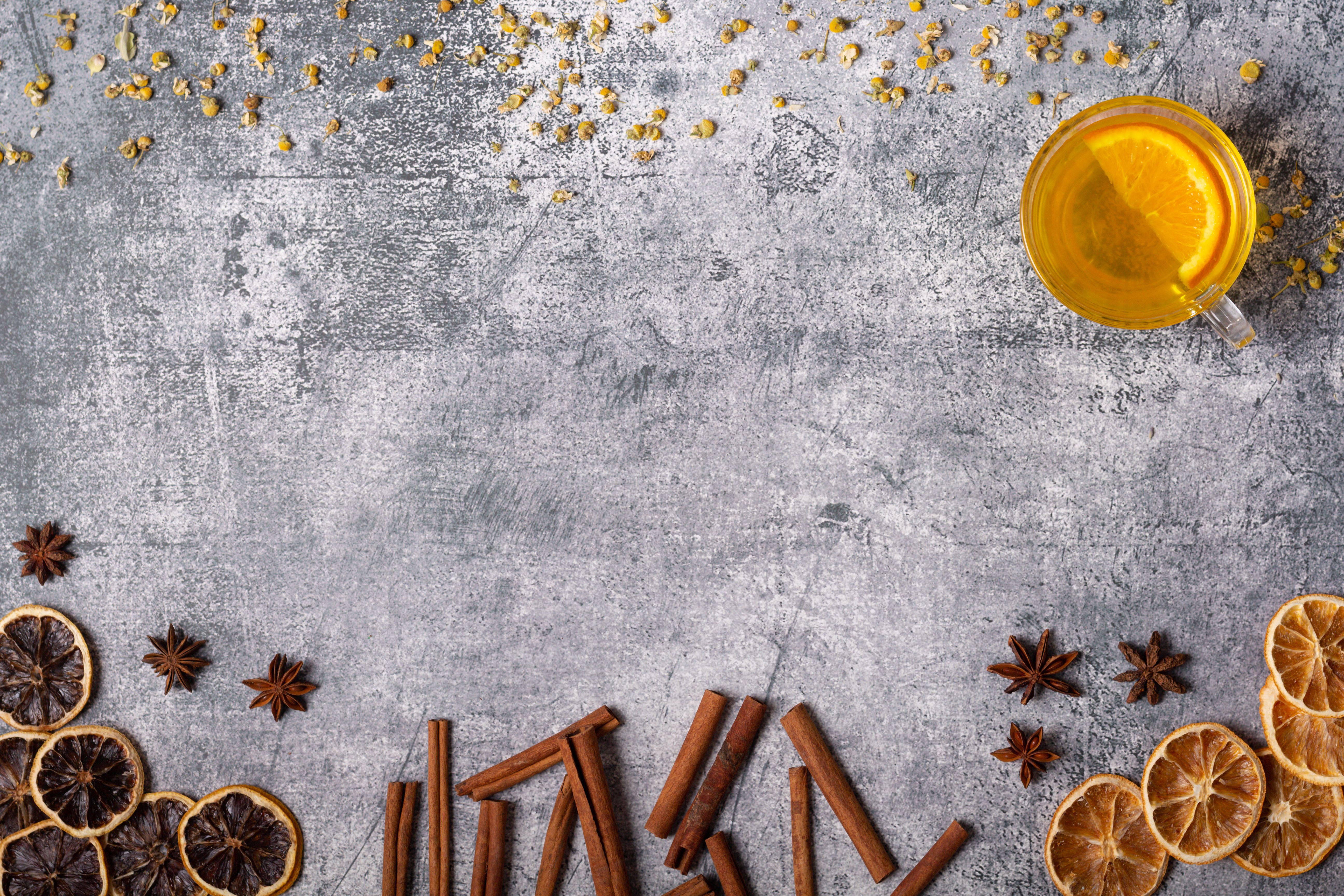 A warm cup of herbal tea with dried oranges, cinnamon sticks, and star anise on a rustic countertop.