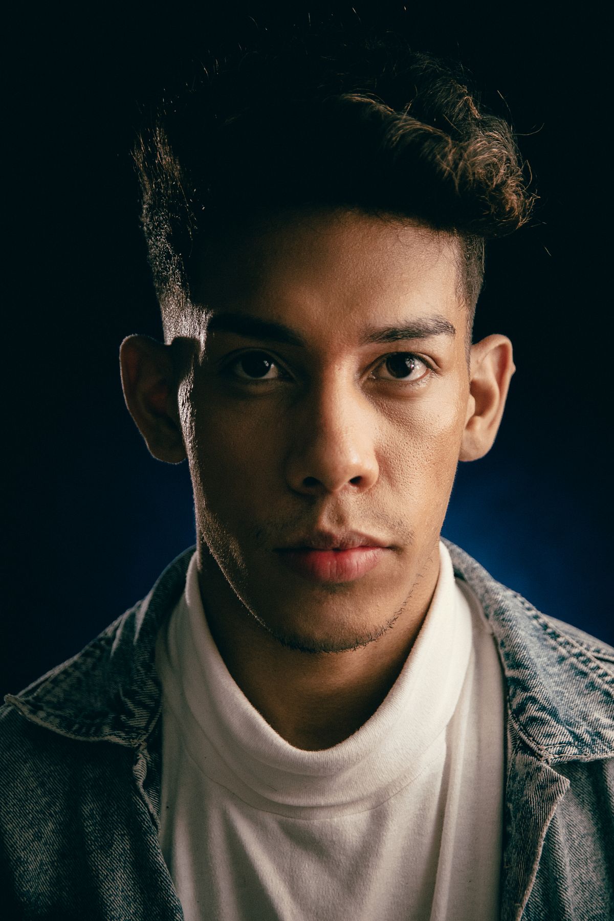 Portrait of a young man in a denim jacket under dramatic lighting