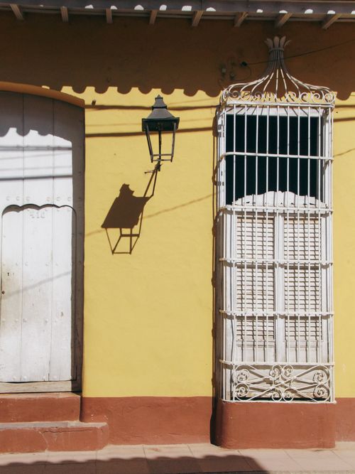 Free A vintage yellow wall featuring a wrought iron window and a classic lamp casting a shadow. Stock Photo