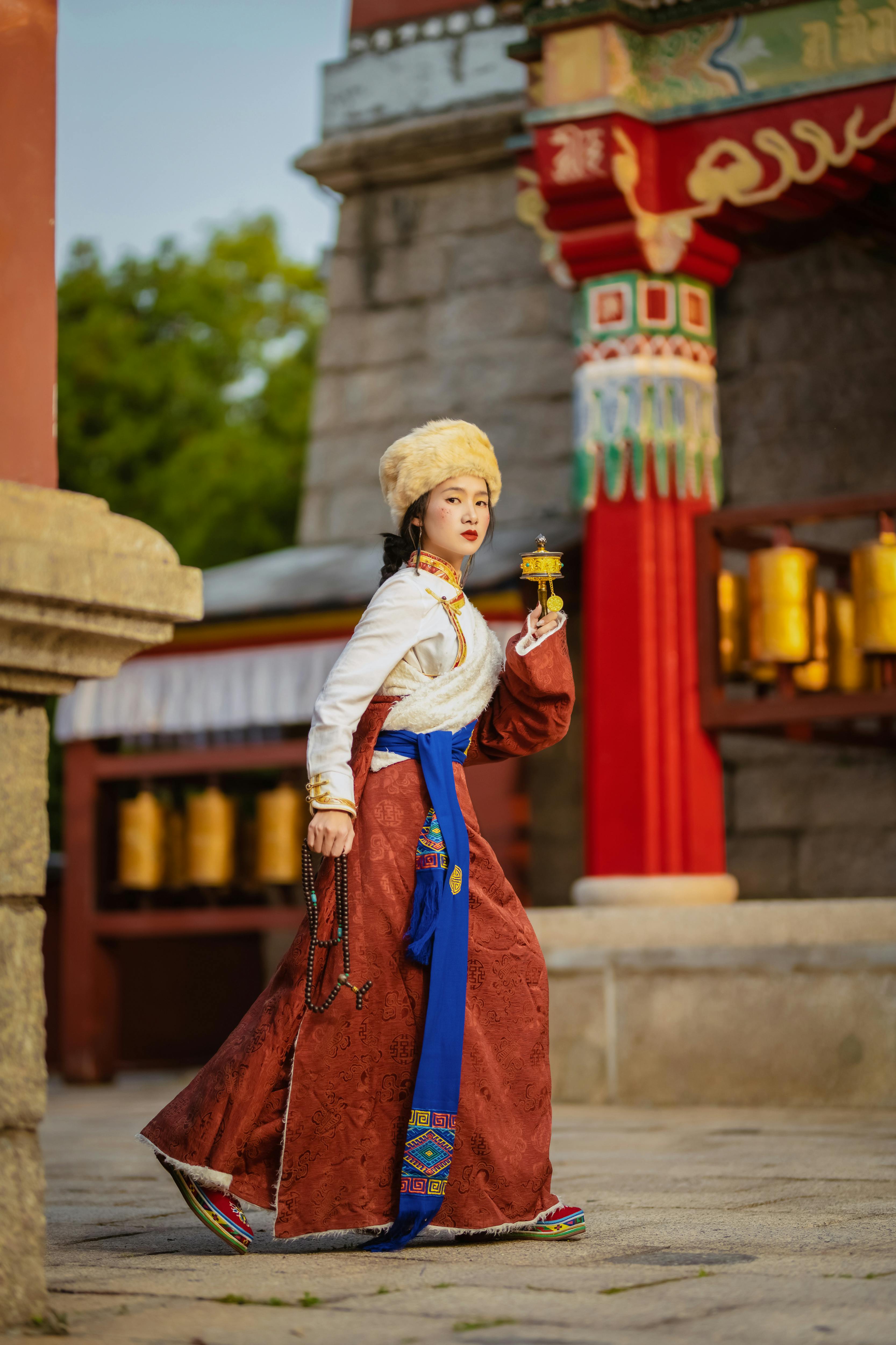 Woman in elegant traditional attire holding prayer wheel at ornate temple with colorful details.