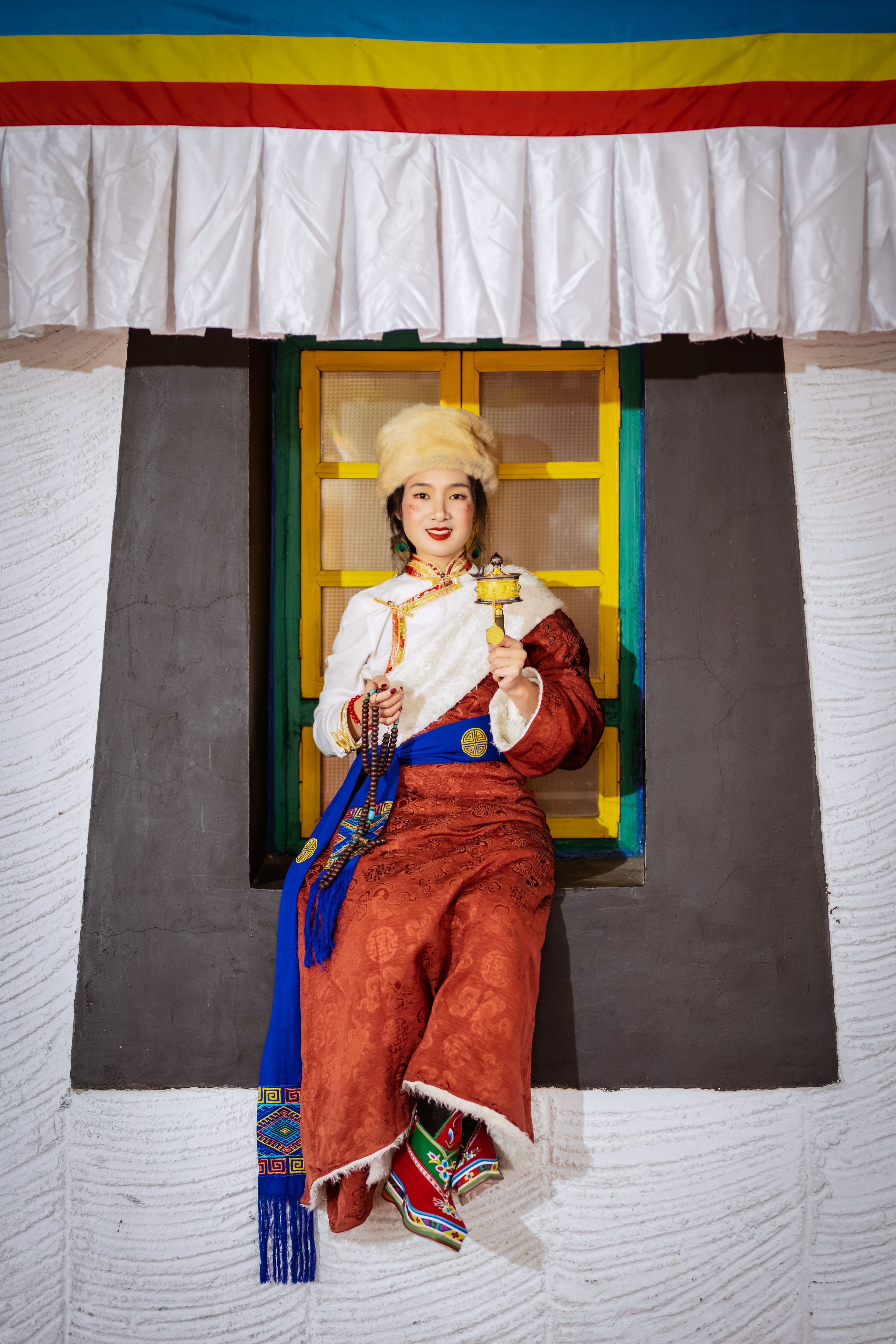 Woman in colorful traditional clothing seated on a decorated window ledge.