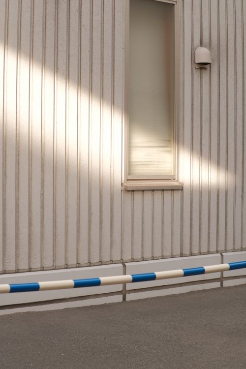 Free A minimalist view of a white building facade with a window, railing, and an asphalt road. Stock Photo