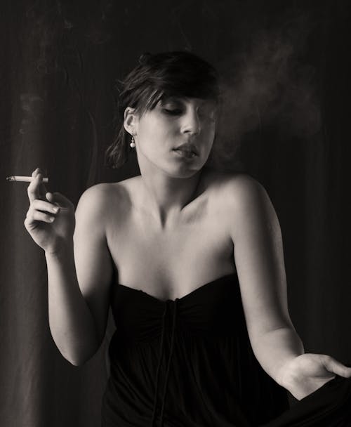 A woman in a black dress smoking a cigarette