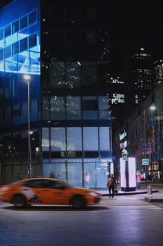 Dynamic city street at night featuring a moving orange taxi and illuminated skyscrapers under a clear night sky.