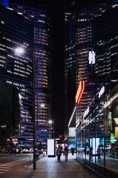 Urban cityscape at night with illuminated buildings and bustling sidewalks.
