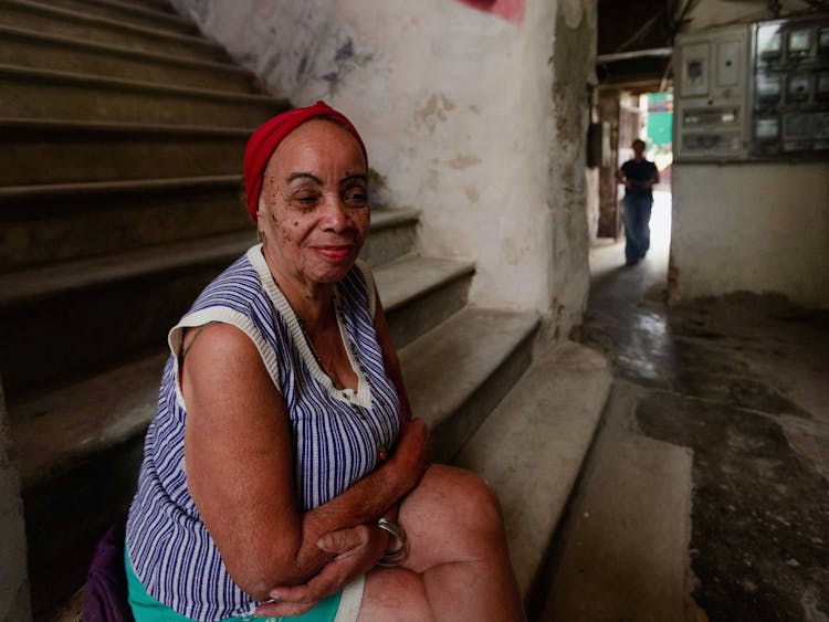 Old Woman Sitting On Stairs In House