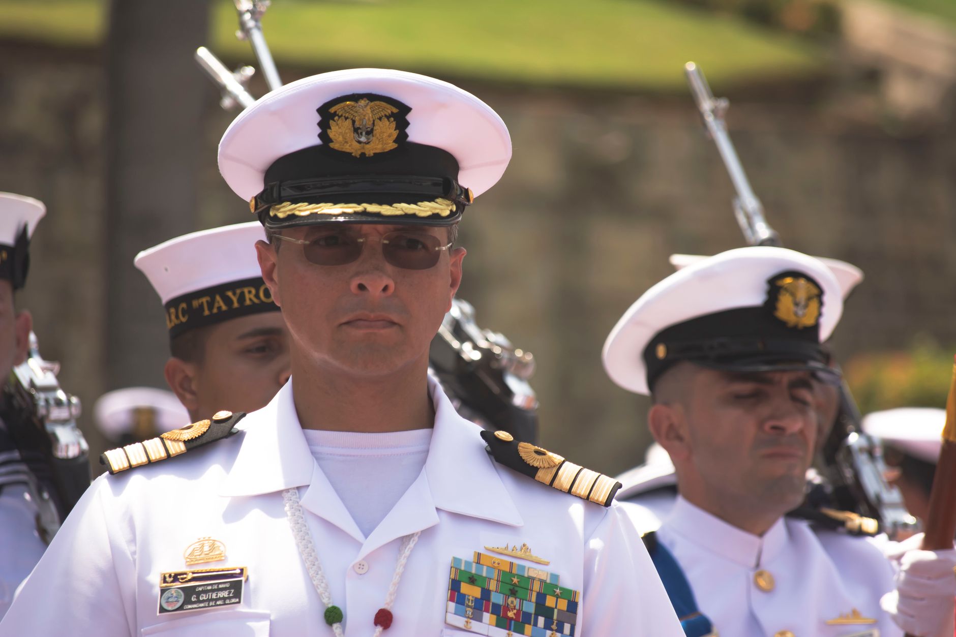 Group of navy officers in white uniforms participating in a formal ceremony outdoors.