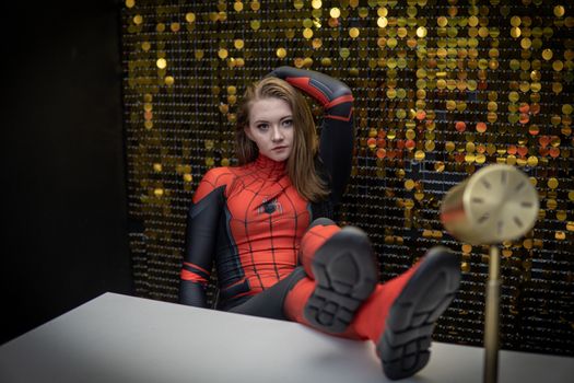 Cosplayer dressed as Spiderman relaxing with feet on the table against a decorative wall.
