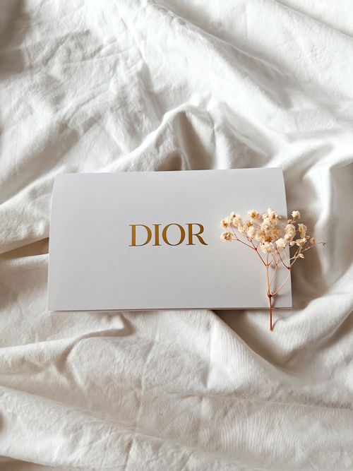 Free Chic Dior envelope on soft fabric, accented by delicate dry flowers for a luxurious touch. Stock Photo