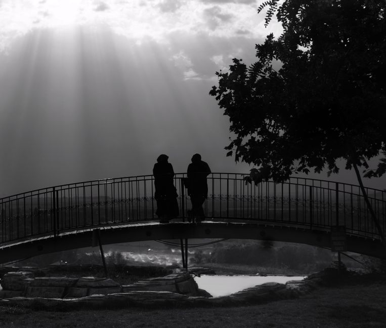 A captivating black and white image of people on a bridge with dramatic sunbeams.