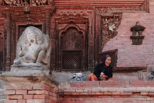 Free Elderly woman sitting next to a temple statue, showcasing cultural heritage. Stock Photo
