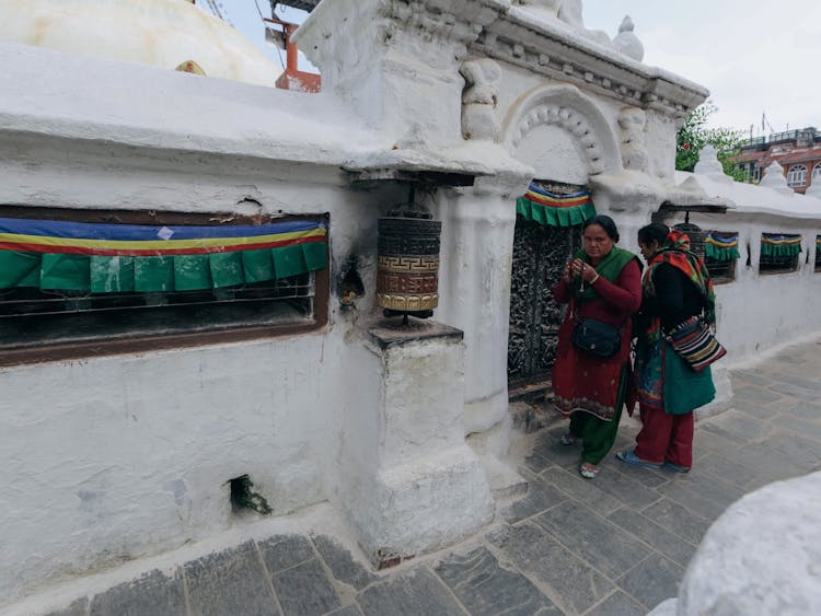 Women Standing Near Building Entrance In White Wall