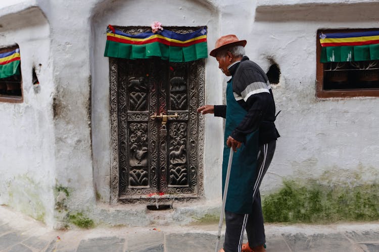 Elderly Man In Hat On Street In Town With Ornamented Door Near