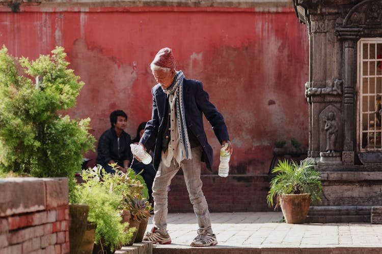 Elderly Man Watering Potted Plants On Sidewalk